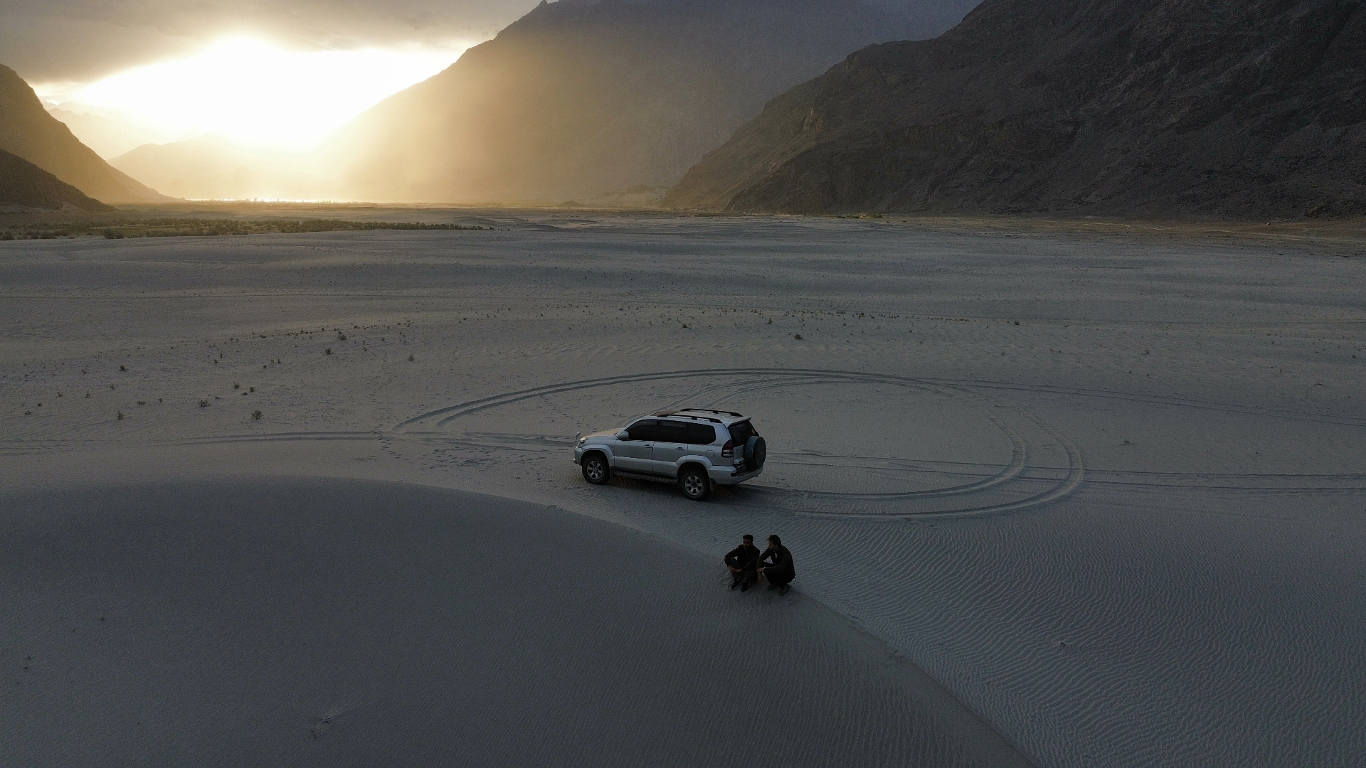 A Land Cruiser parked on a sand dune in the Sarfaranga Cold Desert at sunset, with the Karakoram mountains behind
